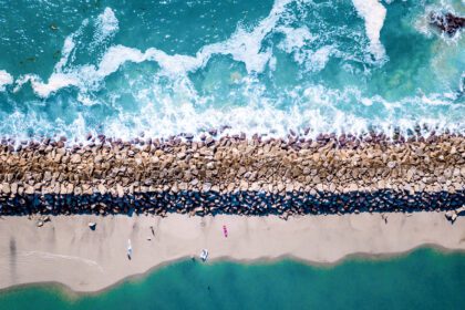A strip of land between two bodies of water shot from above. one side is rocky and the other is an uncrowded beach